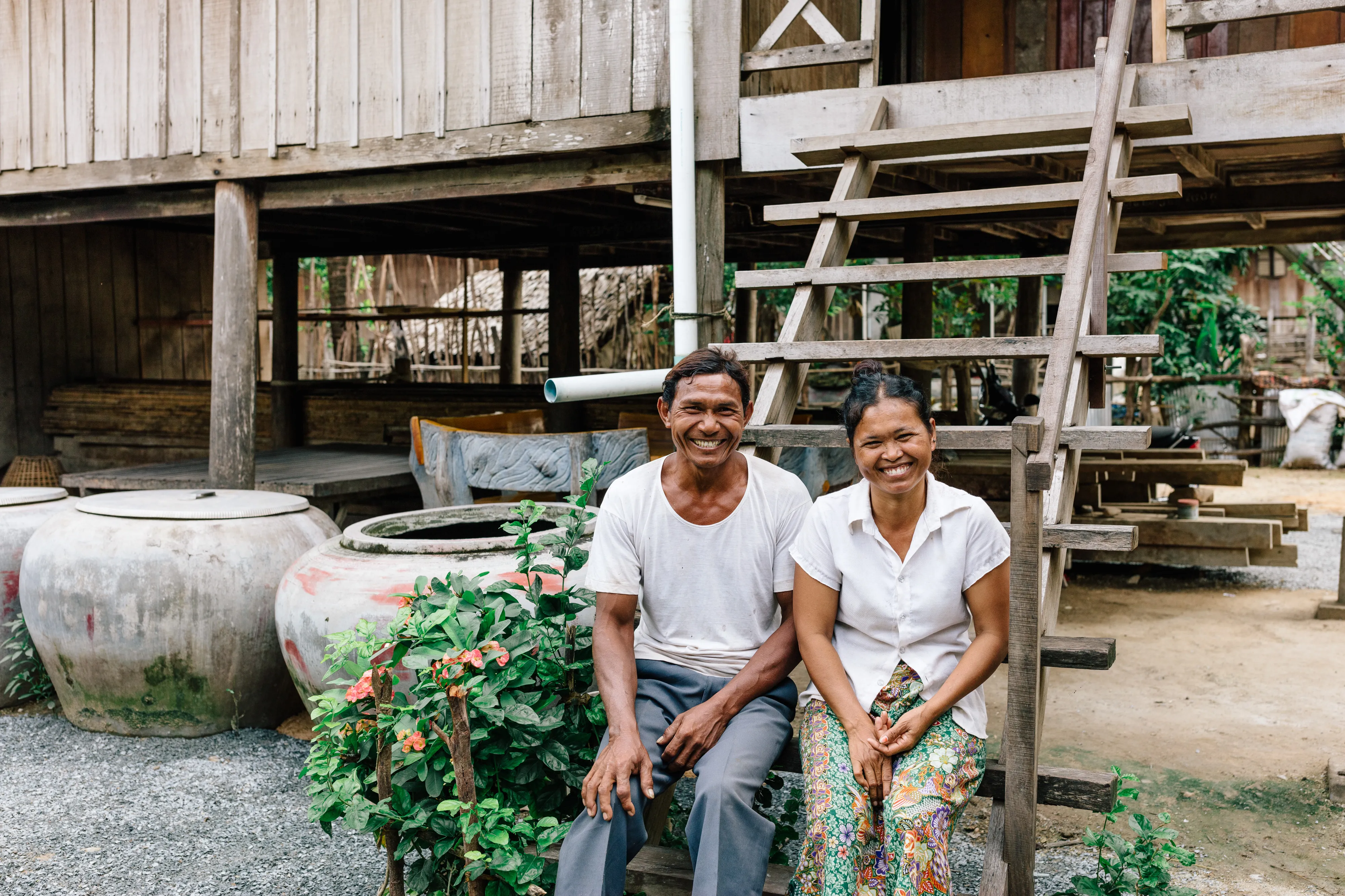Young couple smiling while sitting on the steps outside of their home in Cambodia.