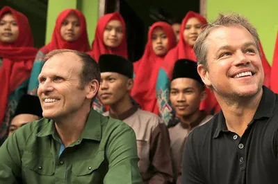 Water.org founders Gary White and Matt Damon smiling in front of a group of people.