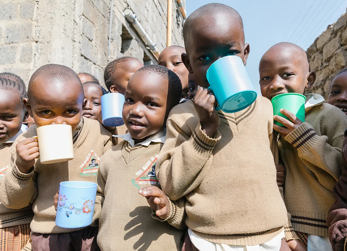 Group of young children in school uniforms drinking water out of cups outside of their school in Kenya.