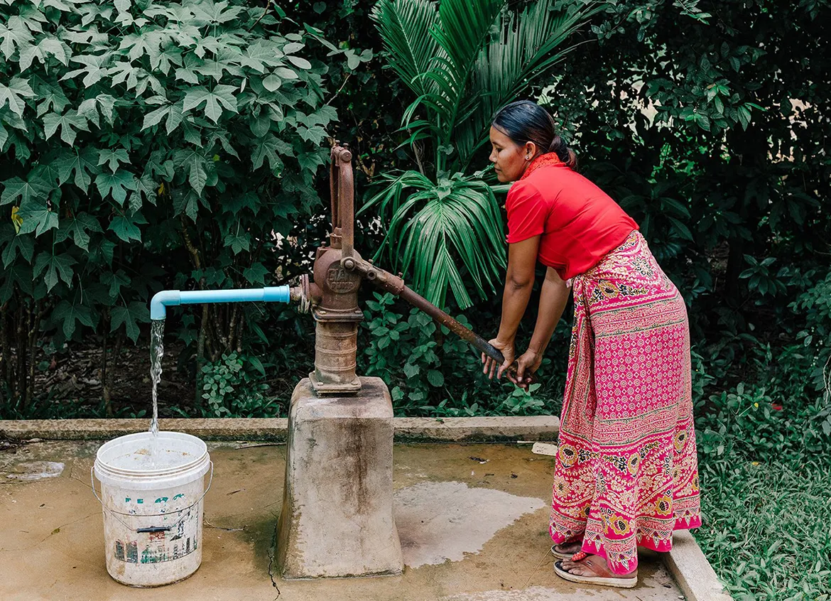 Woman using a water pump to fill up a white bucket.