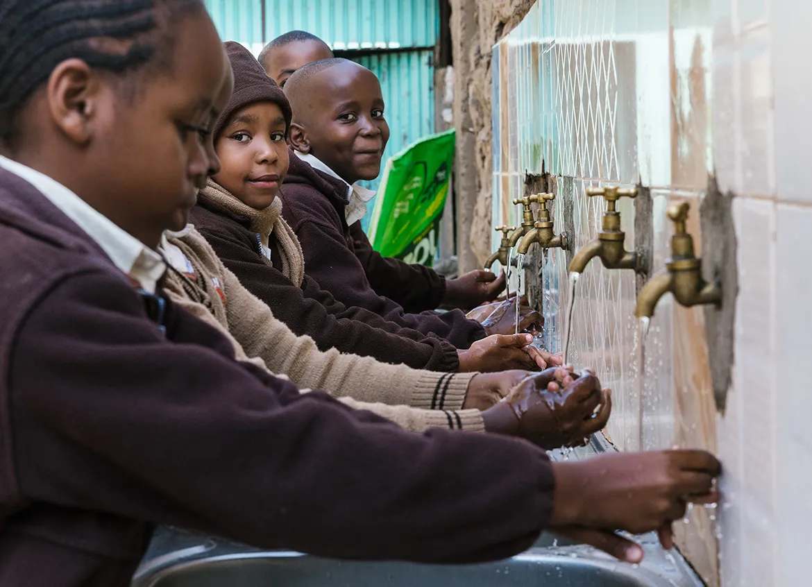 Children wearing school uniforms washing their hands at school.
