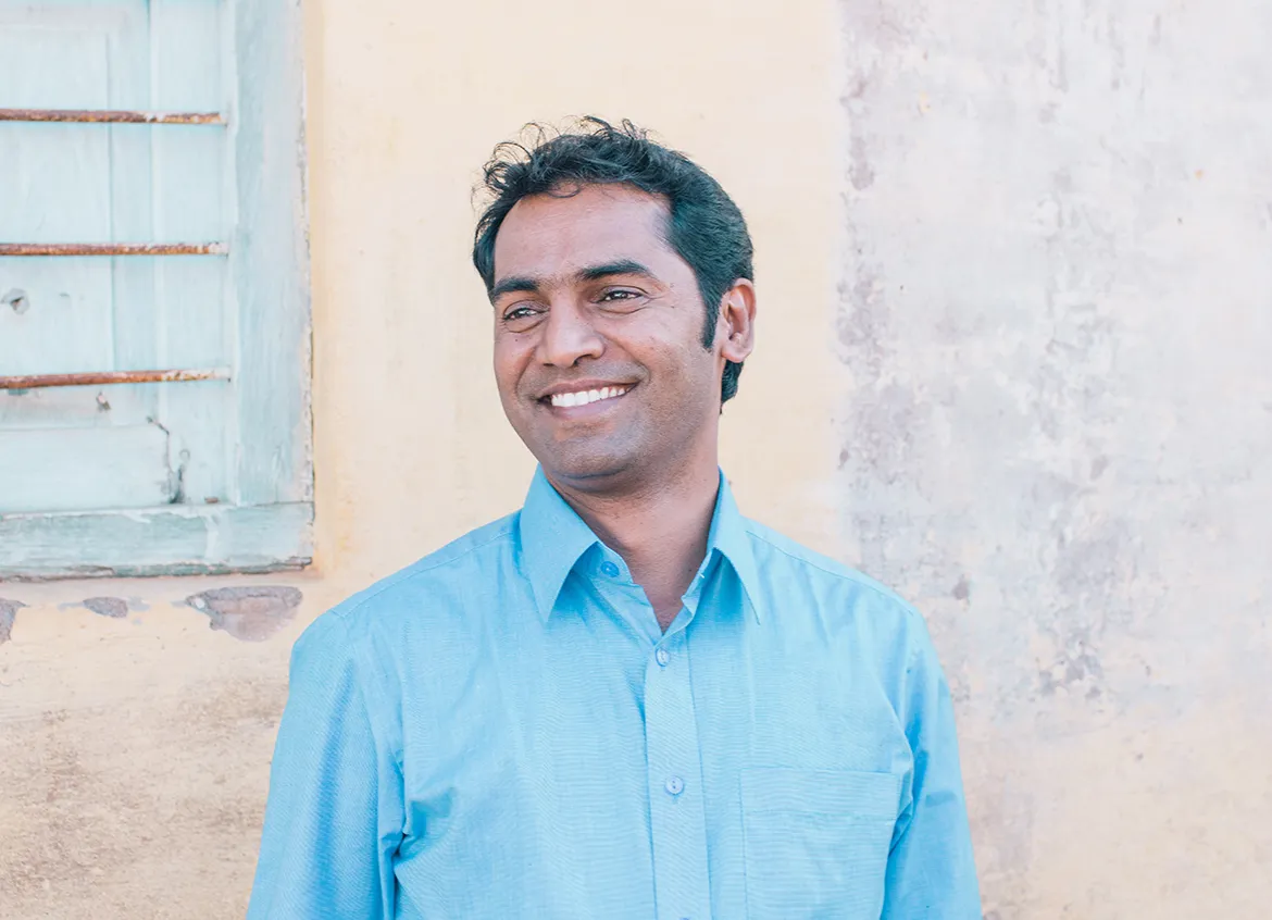 Rev. Fr. D’Ameda, director of the water and sanitation lending program for an organization in India smiling in front of wall.