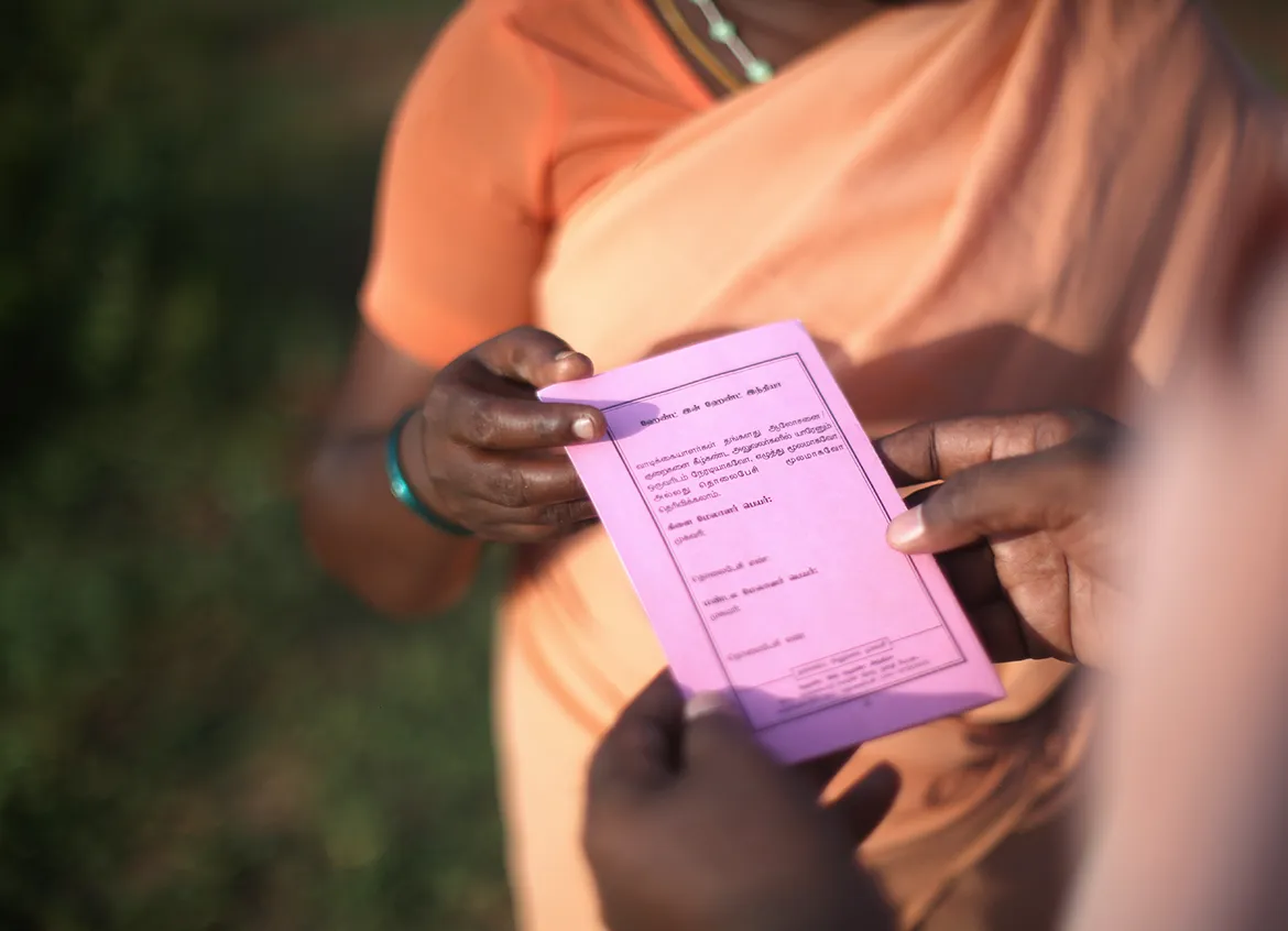 Person holding pink flyer about microfinance solutions in India.